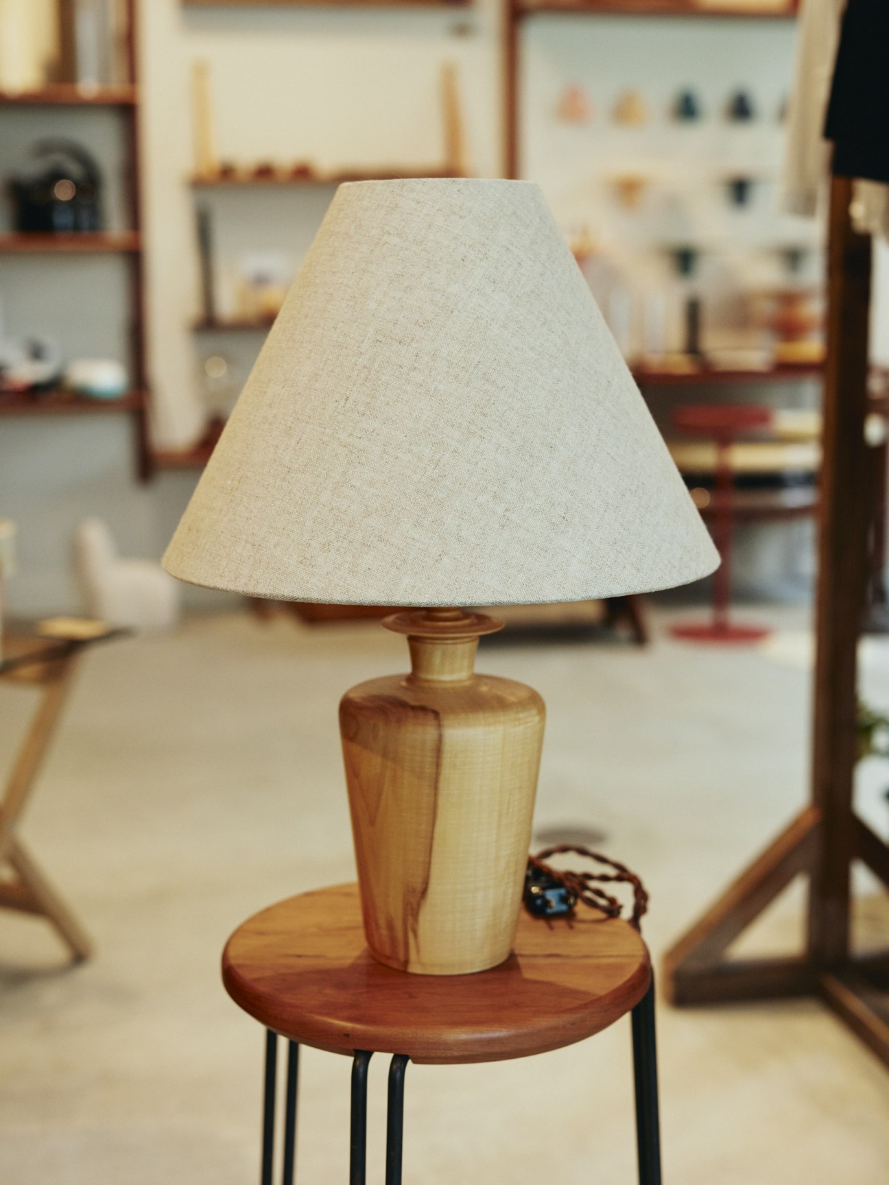 Wooden table lamp with cream linen shade by Inaguma Furniture & Cabinetry displayed in Bullpen shop.