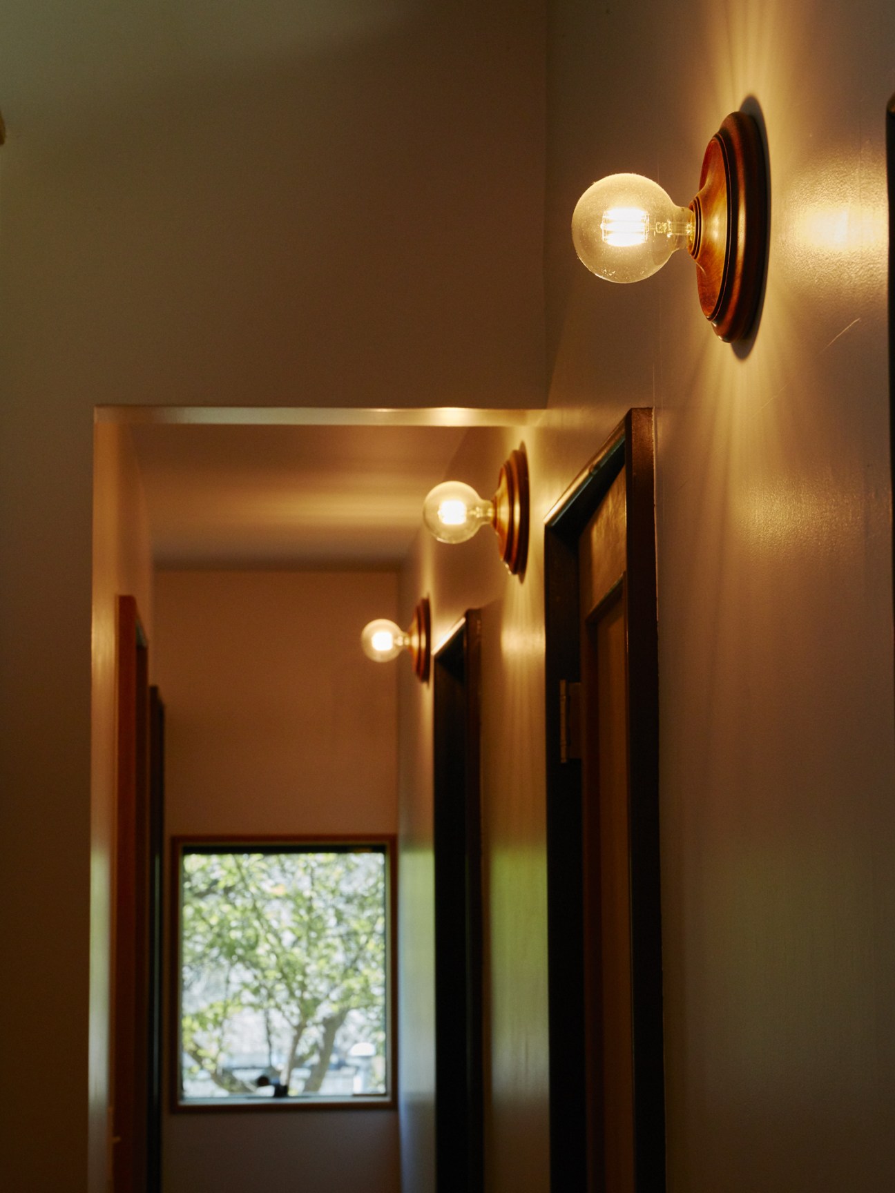 Hallway with wall-mounted lights with wooden backplates and globe bulbs creating warm illumination.