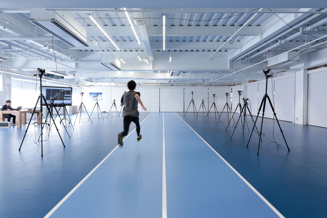 Person running in a motion-capture laboratory with multiple tripod-mounted cameras and tracking equipment