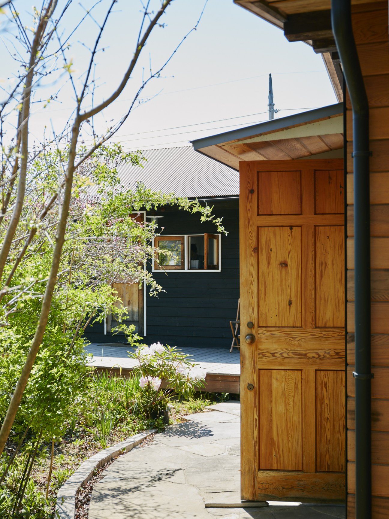 Wooden door and entrance gate with lush green garden plants and a winding stone pathway leading to a renovated house.