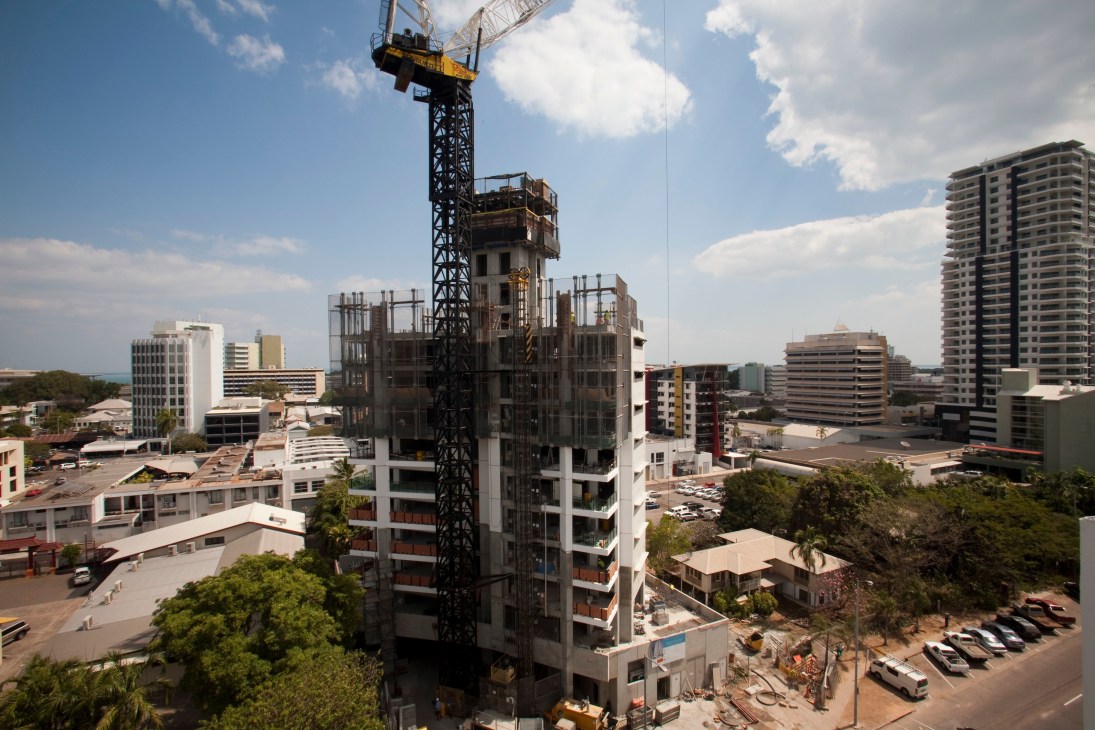 A construction crane towers over a partially built residential building in Darwin's downtown area, surrounded by completed high-rise apartment buildings.