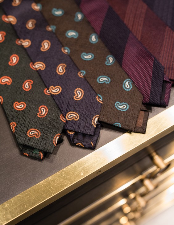 Colorful patterned neckties and scarves displayed on a wooden shelf.