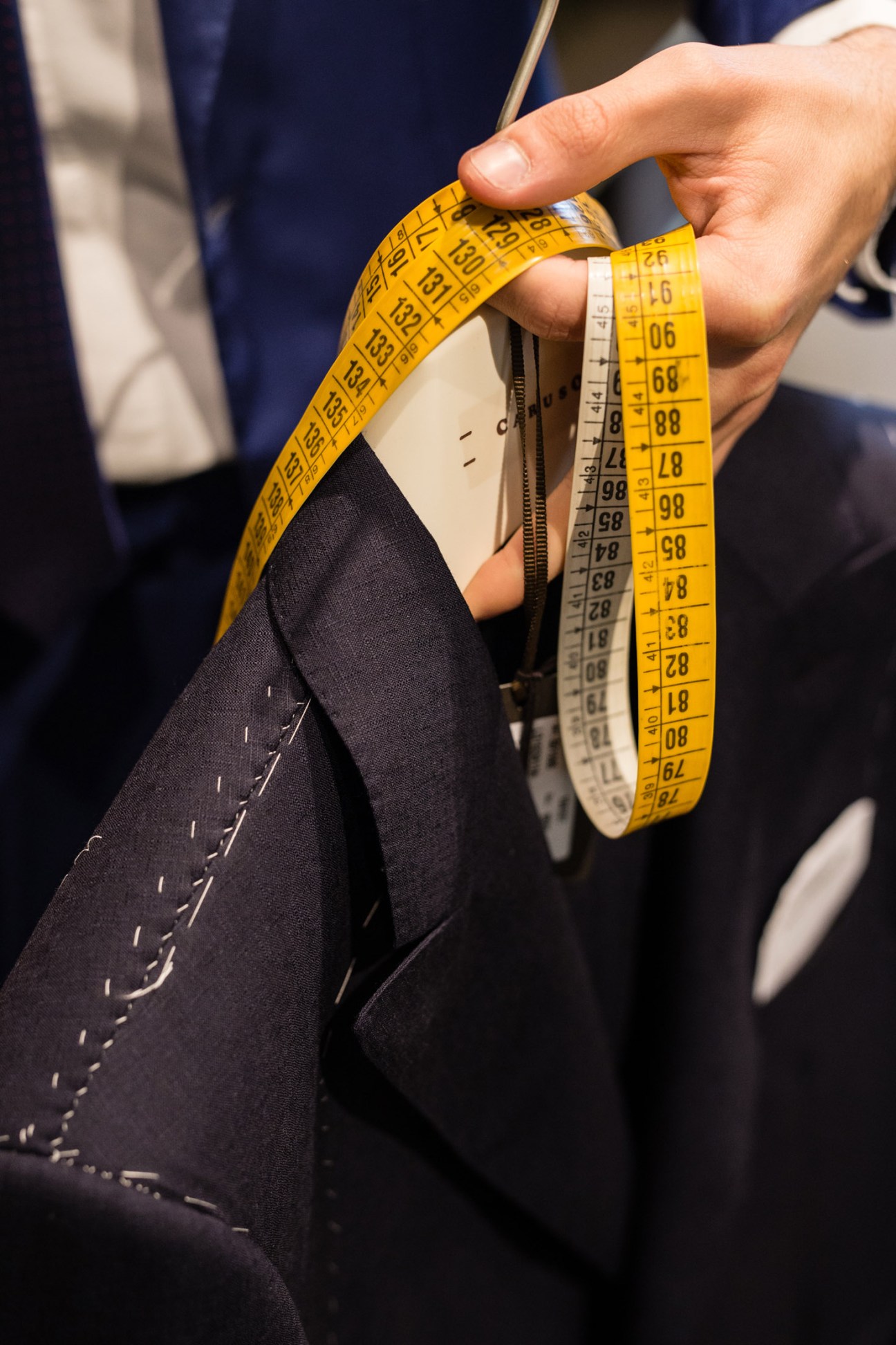 Tailor measuring a navy suit jacket with a yellow measuring tape at Nugnes boutique.