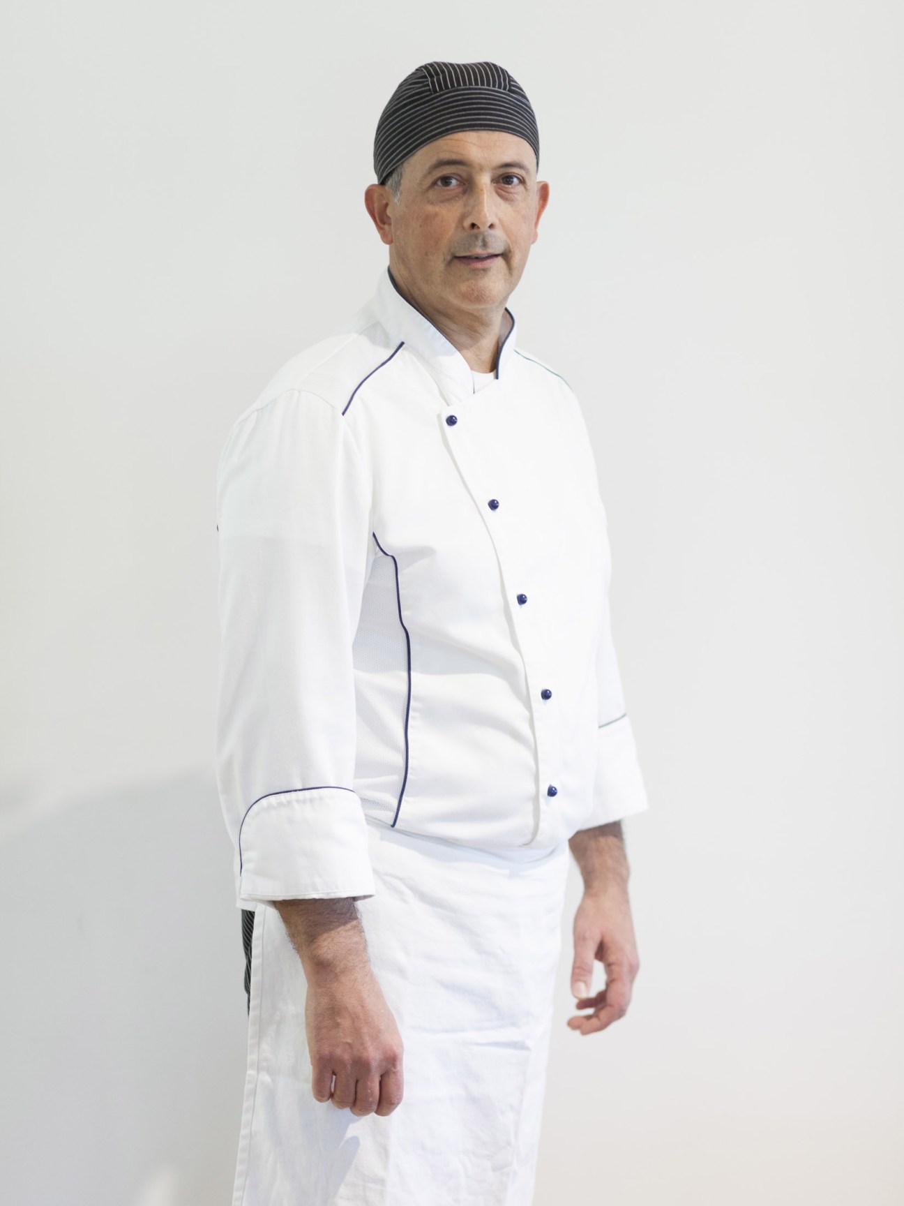 Head chef Moreno Alunni Proietti wearing white chef's jacket with blue trim against white background