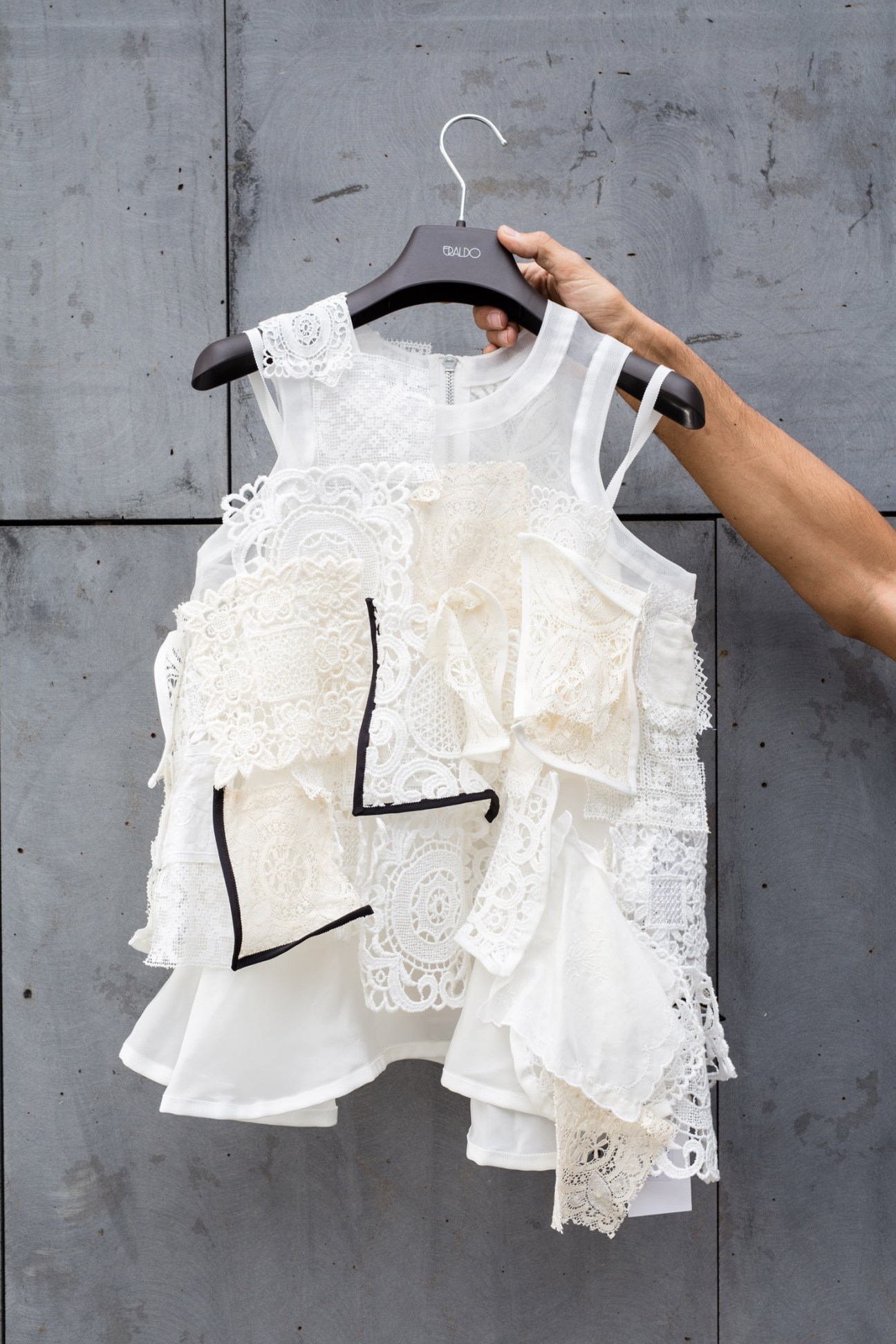 Hand holding Eraldo-branded hanger displaying white lace sleeveless garment with black line drawing