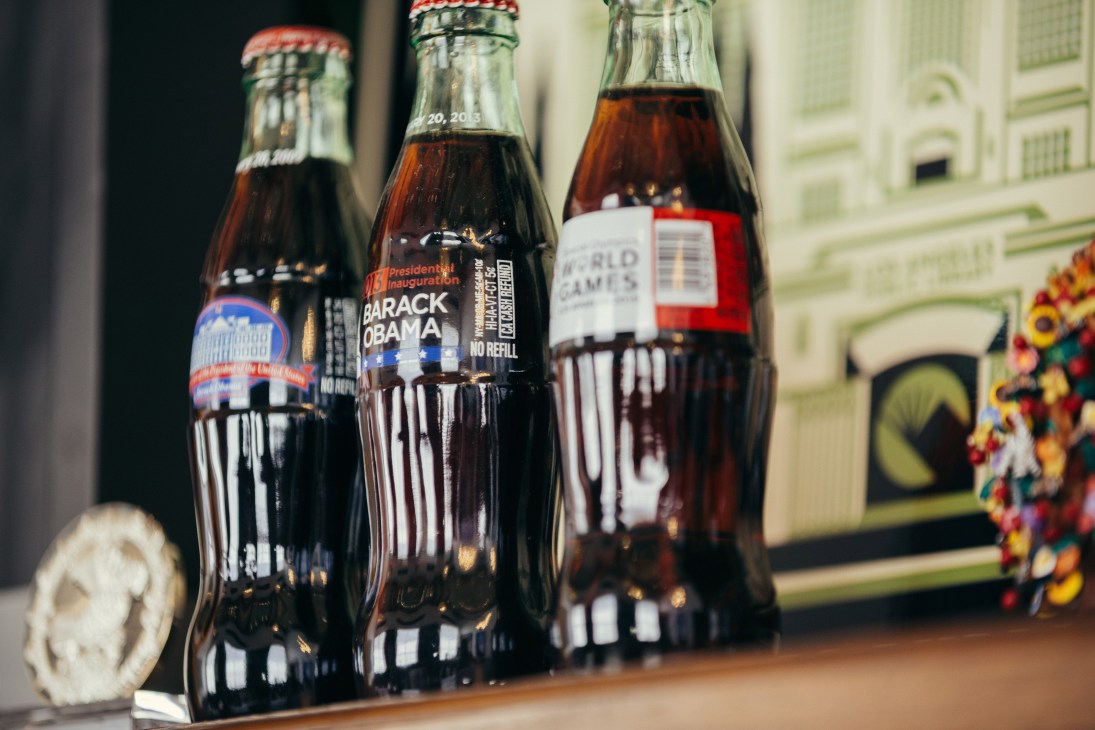 Three Coca-Cola bottles with Barack Obama inauguration commemorative labels displayed on a wooden surface.
