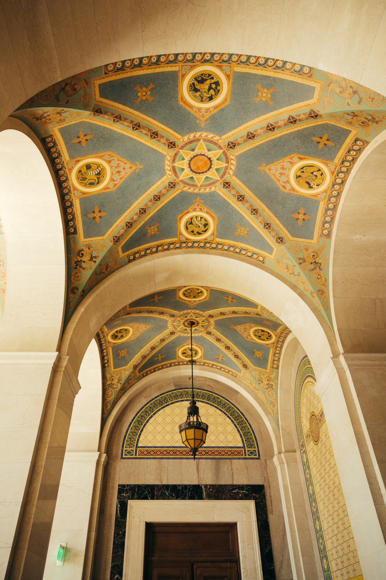 Ornate decorative ceiling with blue and gold geometric patterns and hanging pendant light in 1928 Los Angeles City Hall.