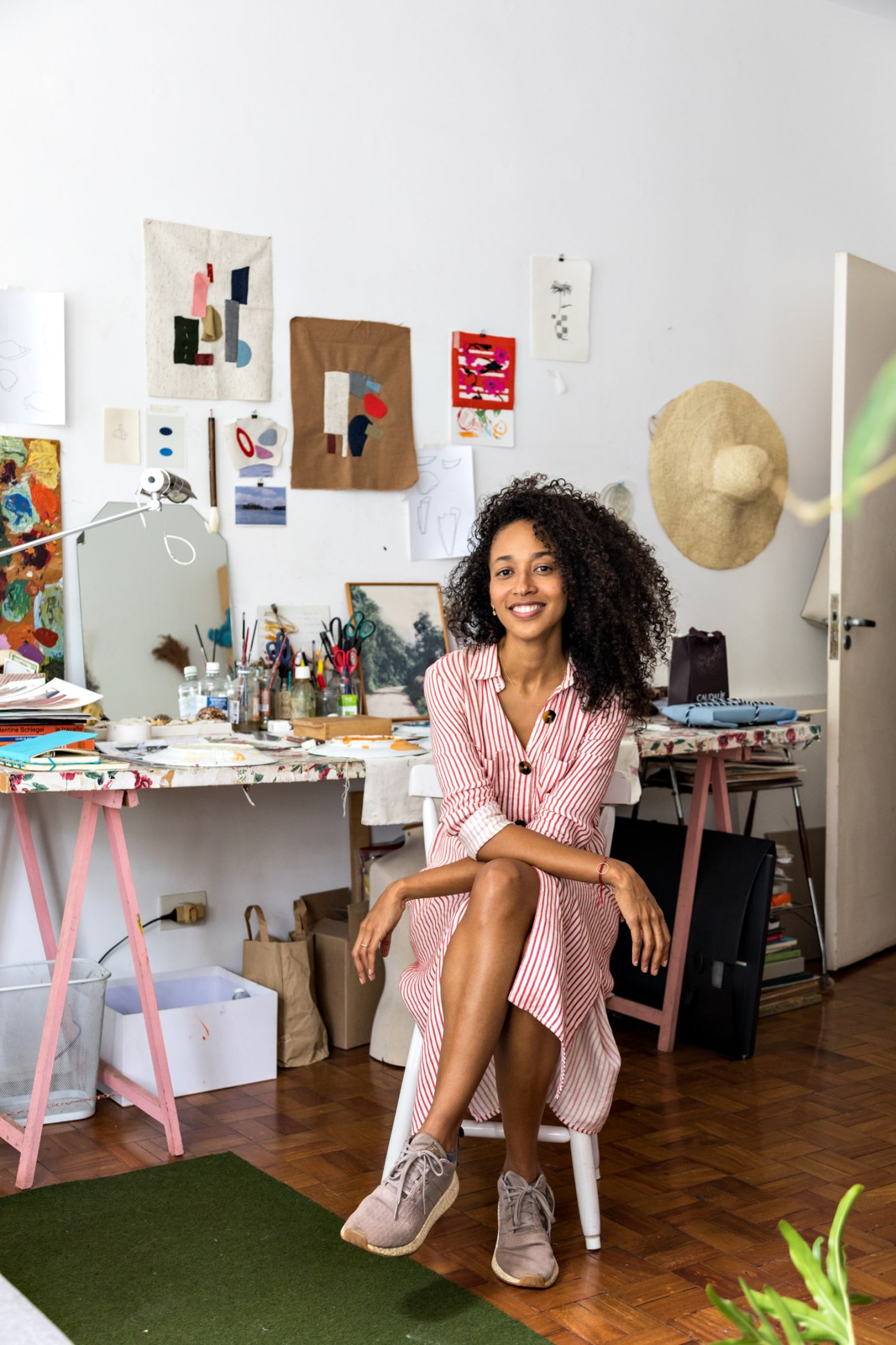 Artist Lane Marinho sitting at her drawing board in her studio apartment, surrounded by colorful artwork and design materials.