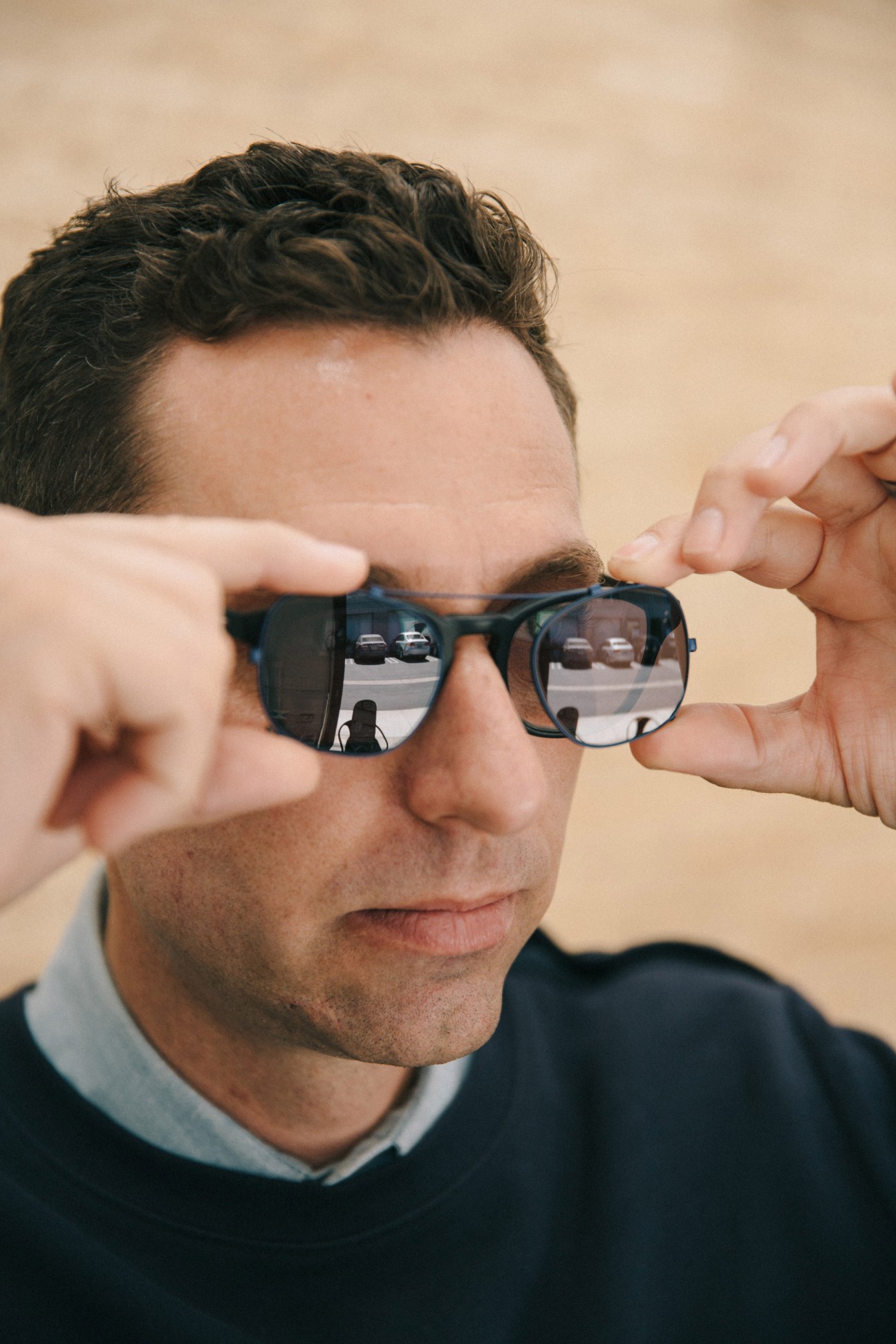 Man holding black-framed sunglasses up to his face with reflections visible in the lenses.