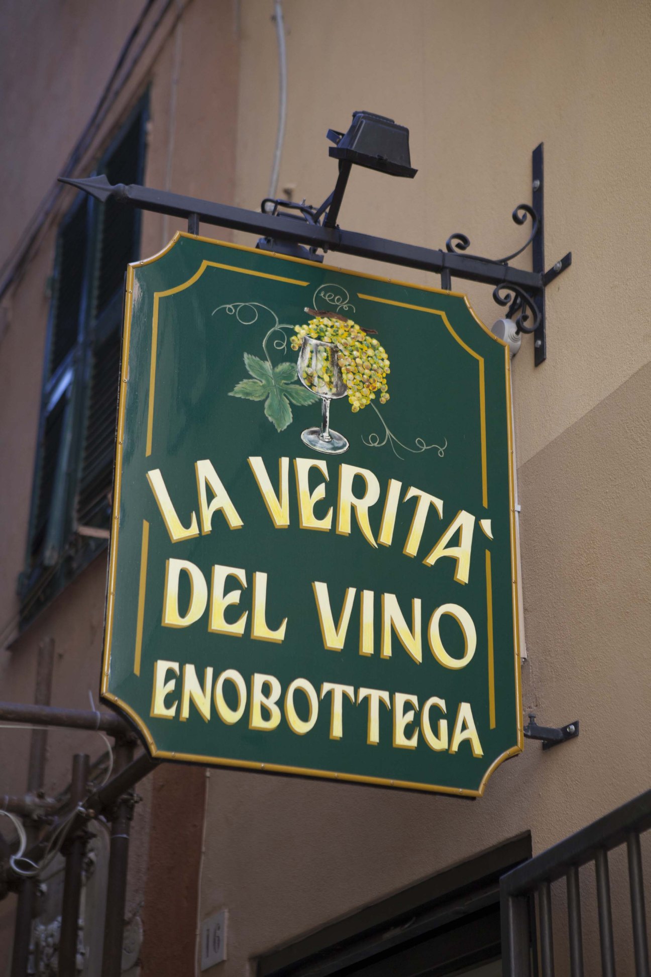 Green hanging sign with yellow lettering and illustration for wine shop La Verità Del Vino Enobottega in Genoa.