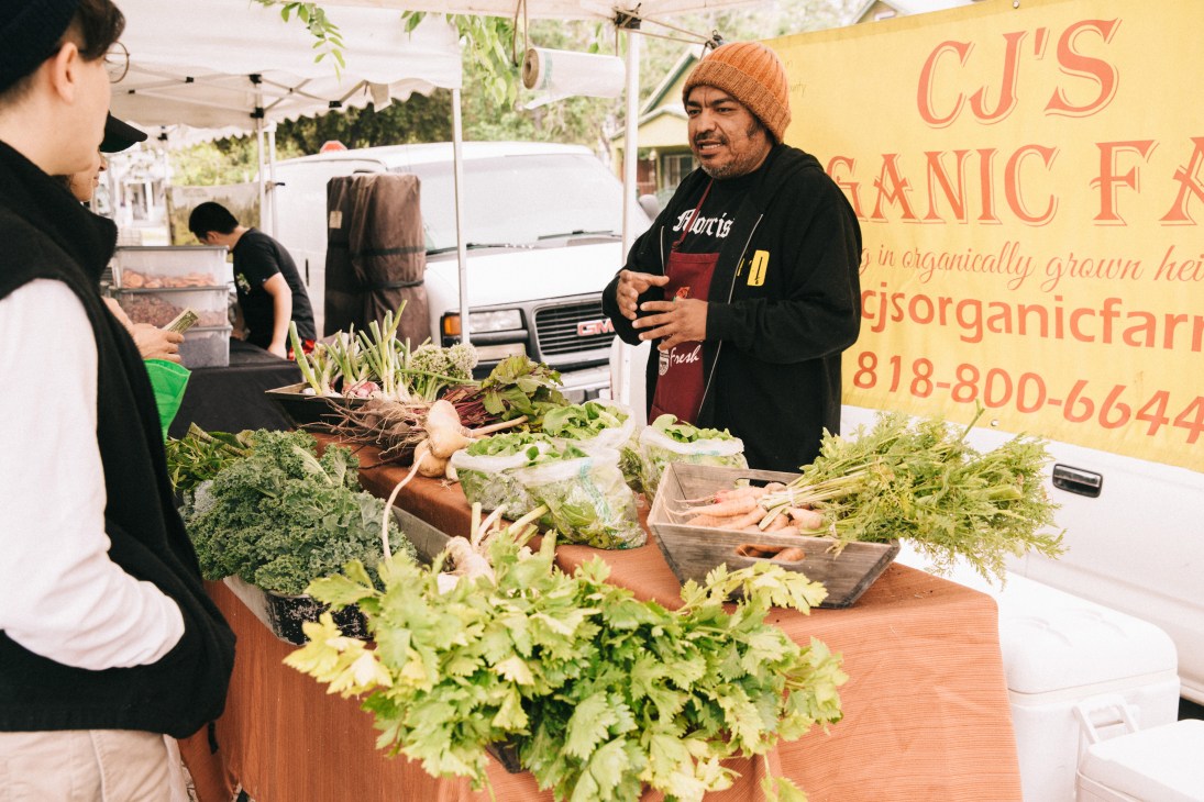 A vendor sells fresh organic vegetables at an LA farmers market stand.