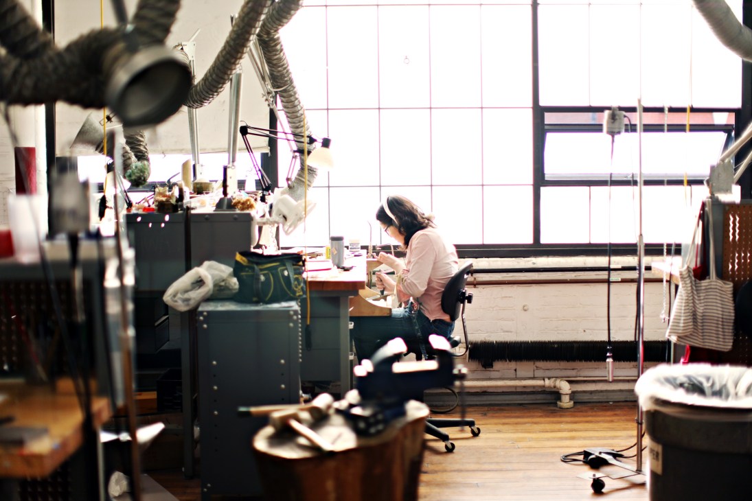 Student working at a jewellery and metalsmithing workstation in a bright studio with large windows.