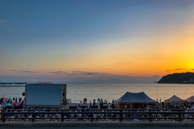 Evening outdoor movie screening with projection screen set up on beach as twilight sets in