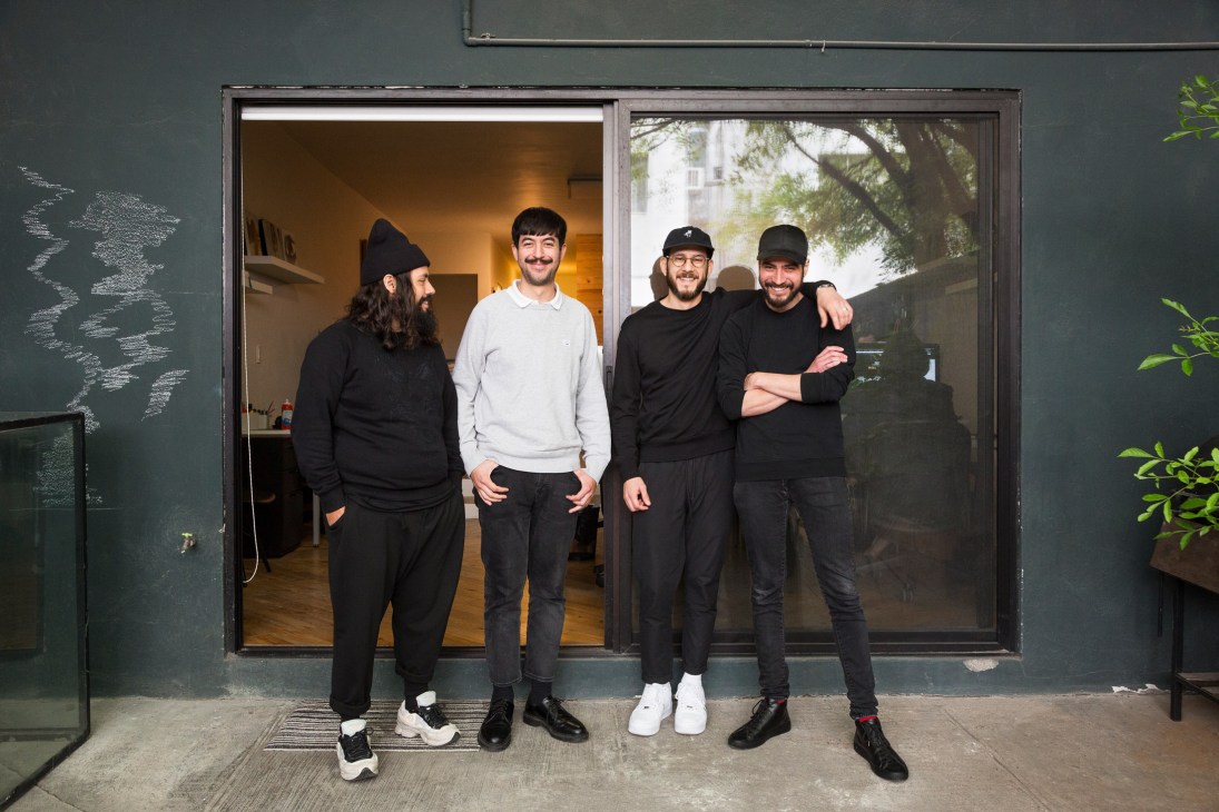 Four men posing outside a studio with a dark green facade and large window display.