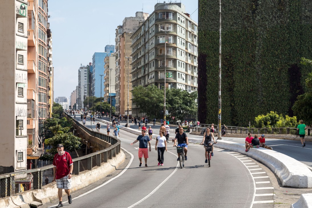 People walking, running and cycling on Minhocão Park, an elevated public space in São Paulo with modern buildings and ivy-covered walls.