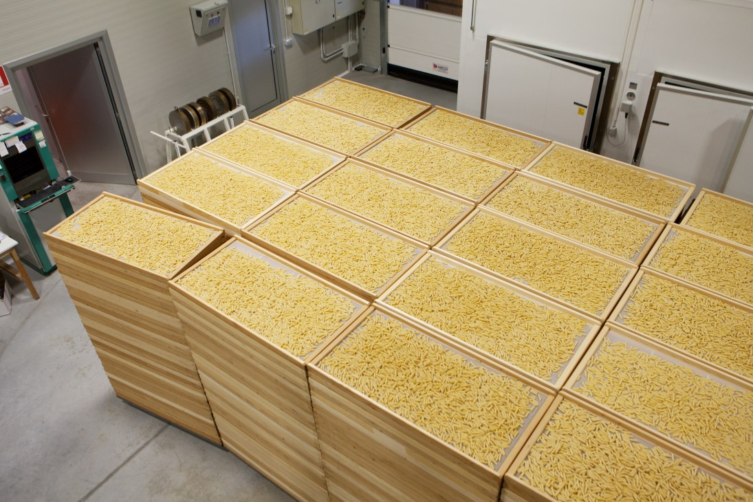 Penne pasta air-drying in wooden crates inside a factory facility.