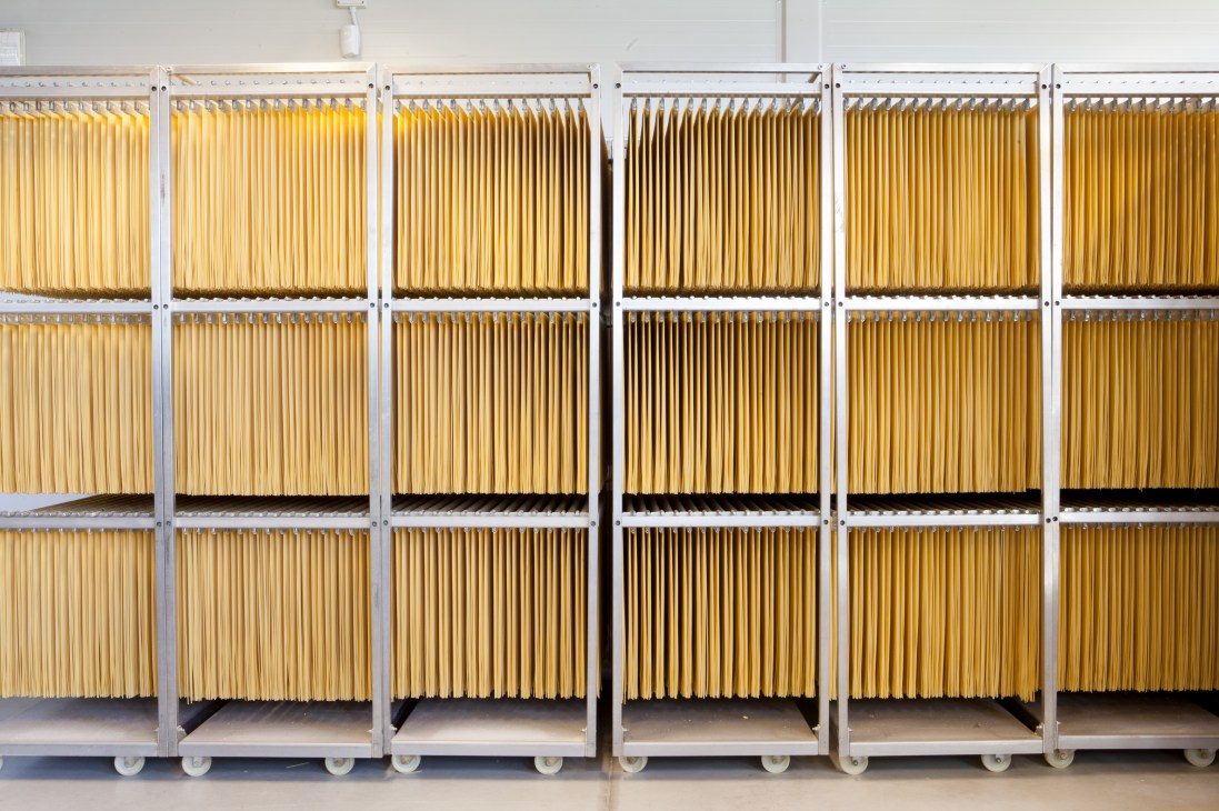 Spaghetti strands hanging in metal drying cabinets for air-drying at low temperature.