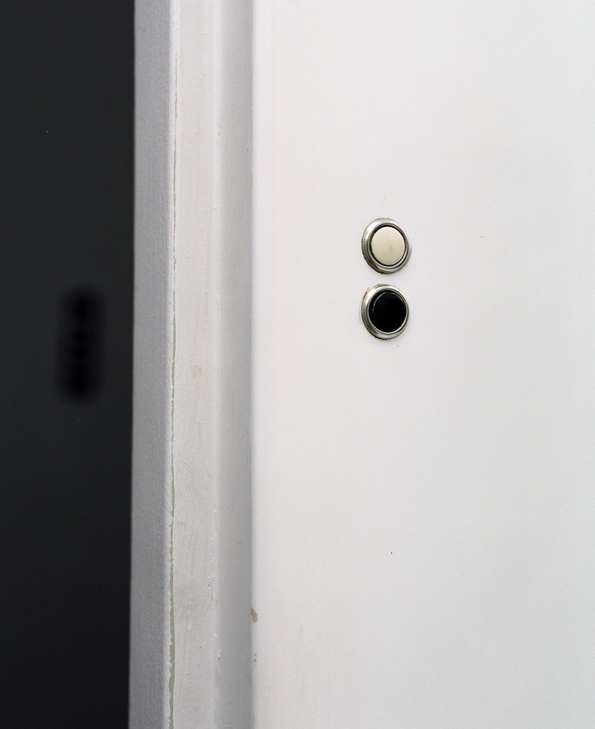 Two original low-voltage circular light switches mounted vertically on a white wall next to a dark vertical beam.