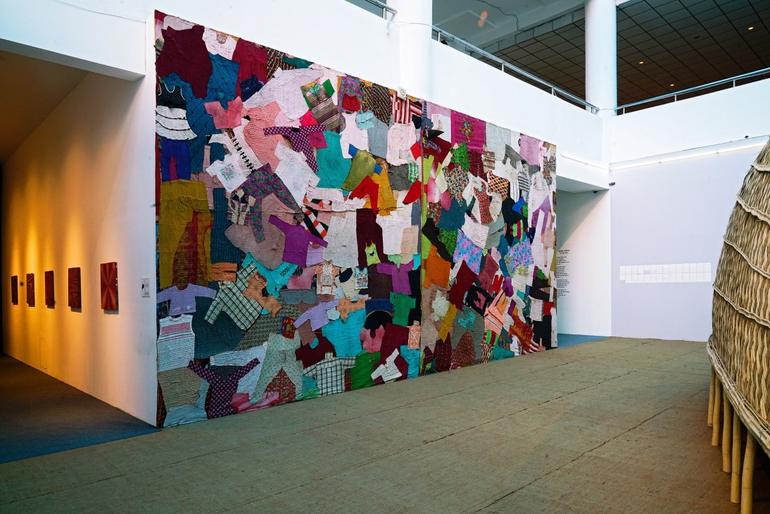 Large colorful textile patchwork artwork displayed in a modern gallery space with white walls and polished concrete floor.