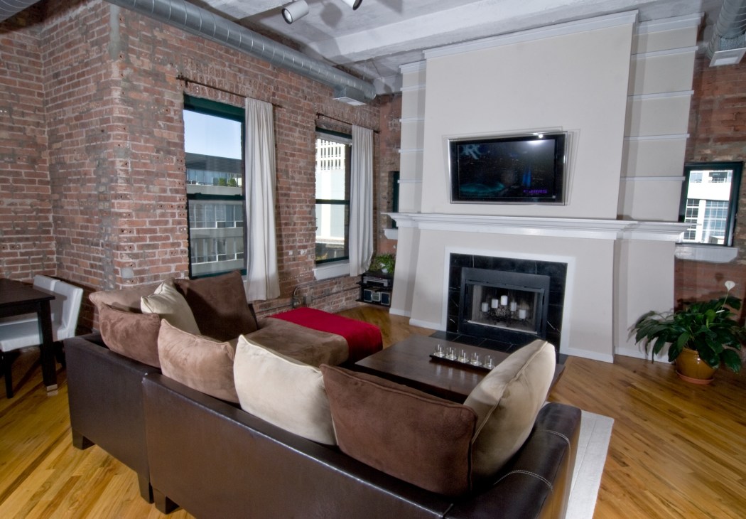 Modern loft apartment with exposed brick wall, leather sofa, fireplace and flat-screen TV.