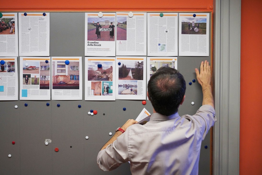 Staff member reviewing magazine layout pages pinned to a board during production