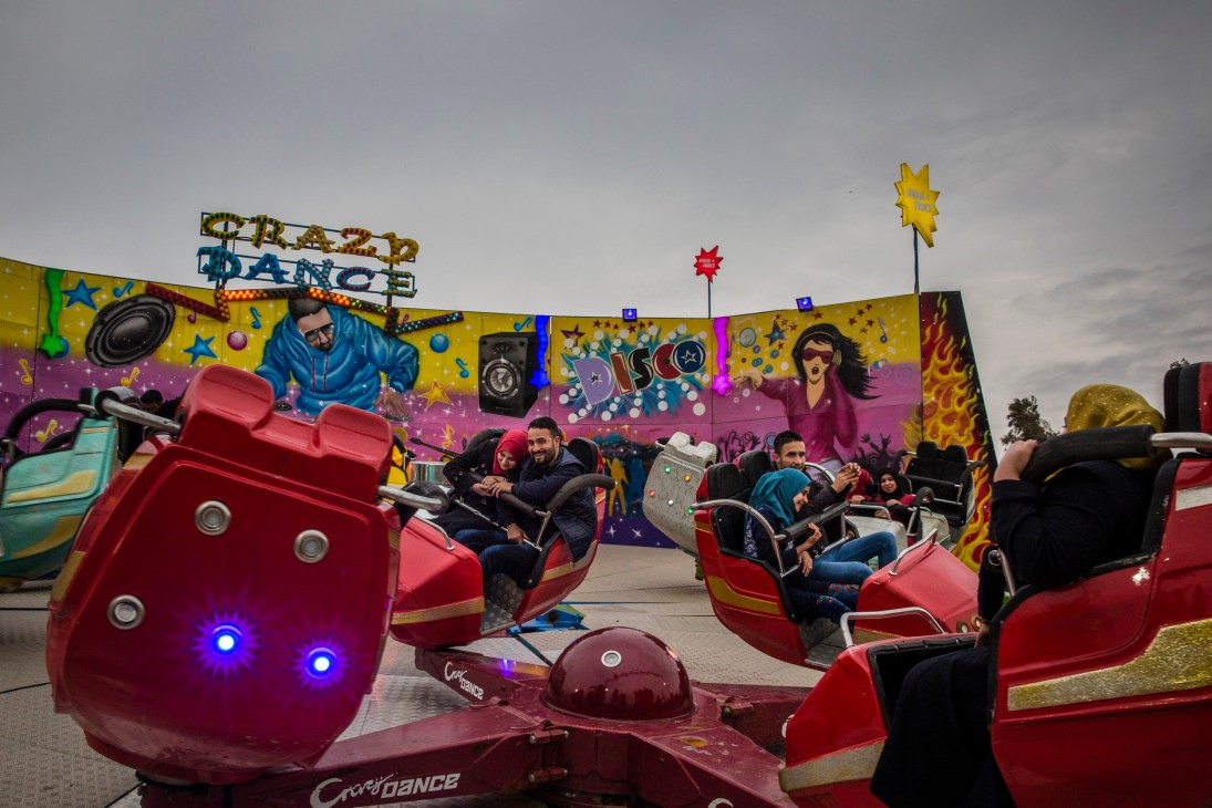 Young couples enjoying a ride on red spinning carnival rides at a newly reopened theme park in East Mosul.