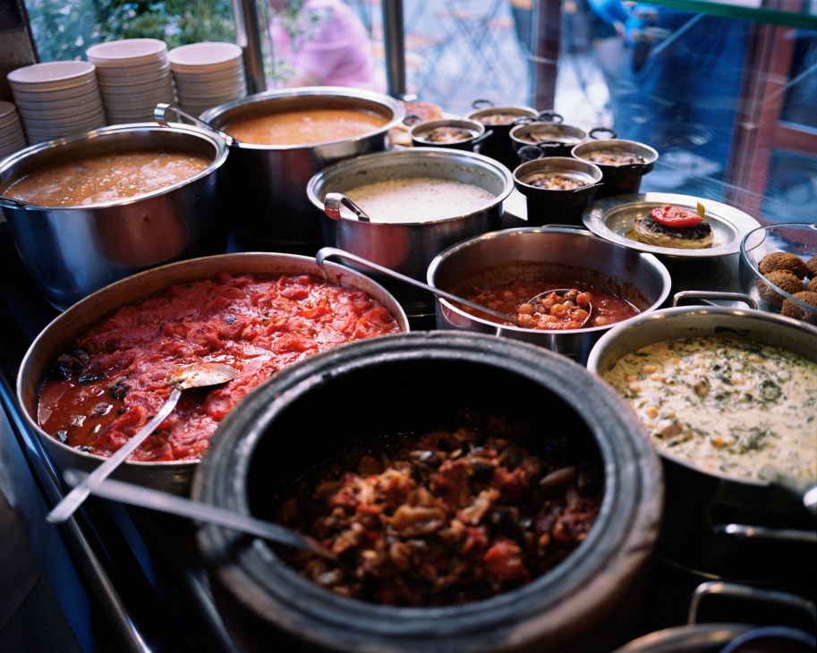 Multiple cooking pots with various dishes displayed in a restaurant kitchen window.