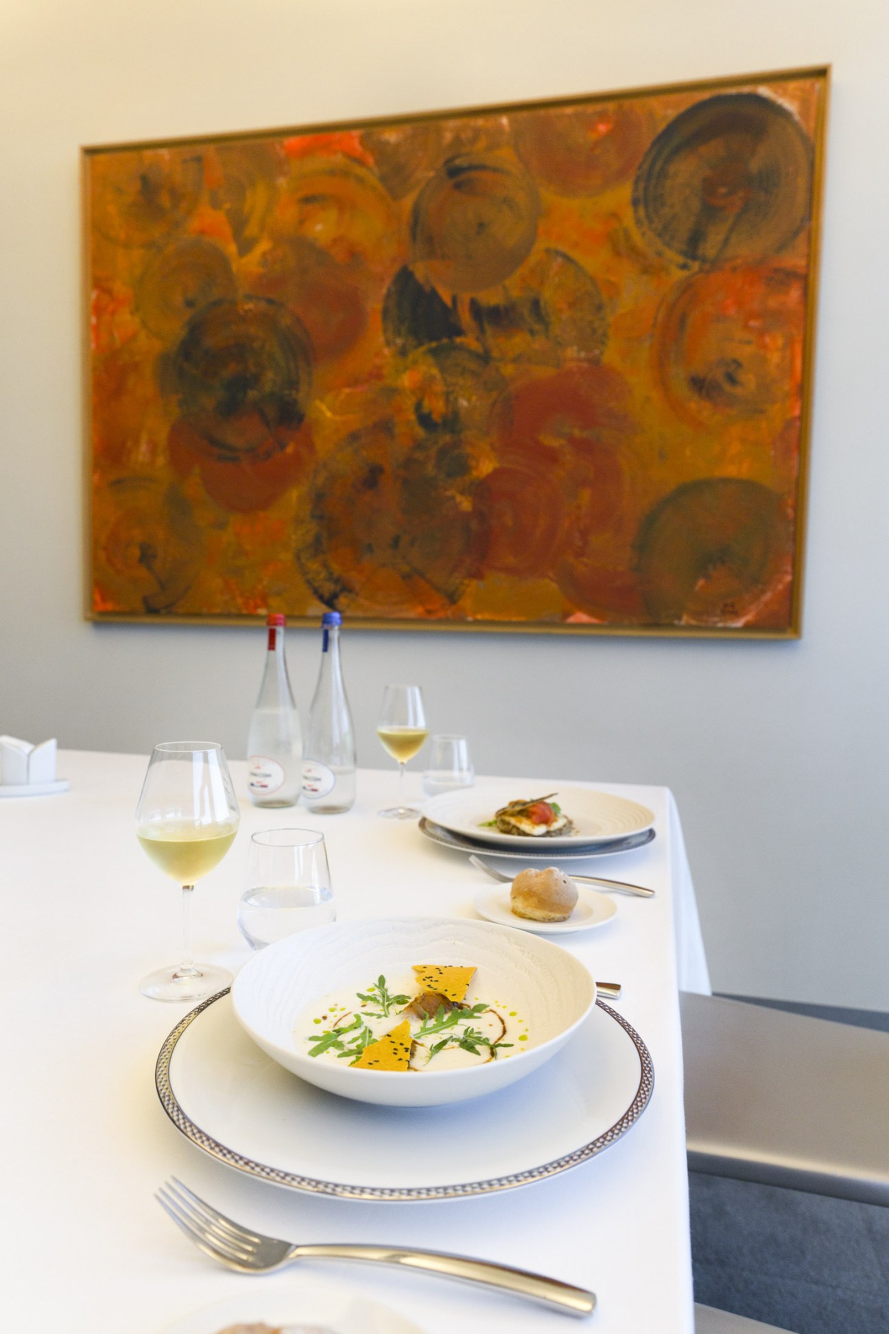Elegantly plated meal with white wine at CMA CGM's executive dining room under abstract artwork.