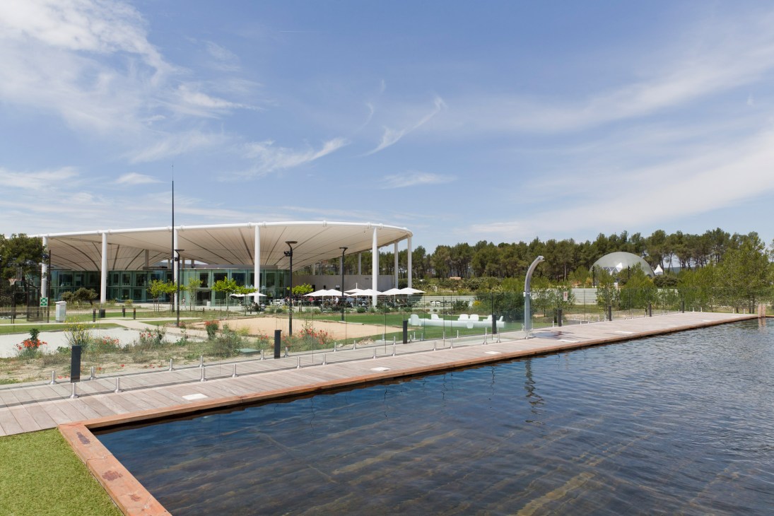 The Camp's modern architecture with white canopy structure overlooking a pond and woodland landscape near Aix-en-Provence.