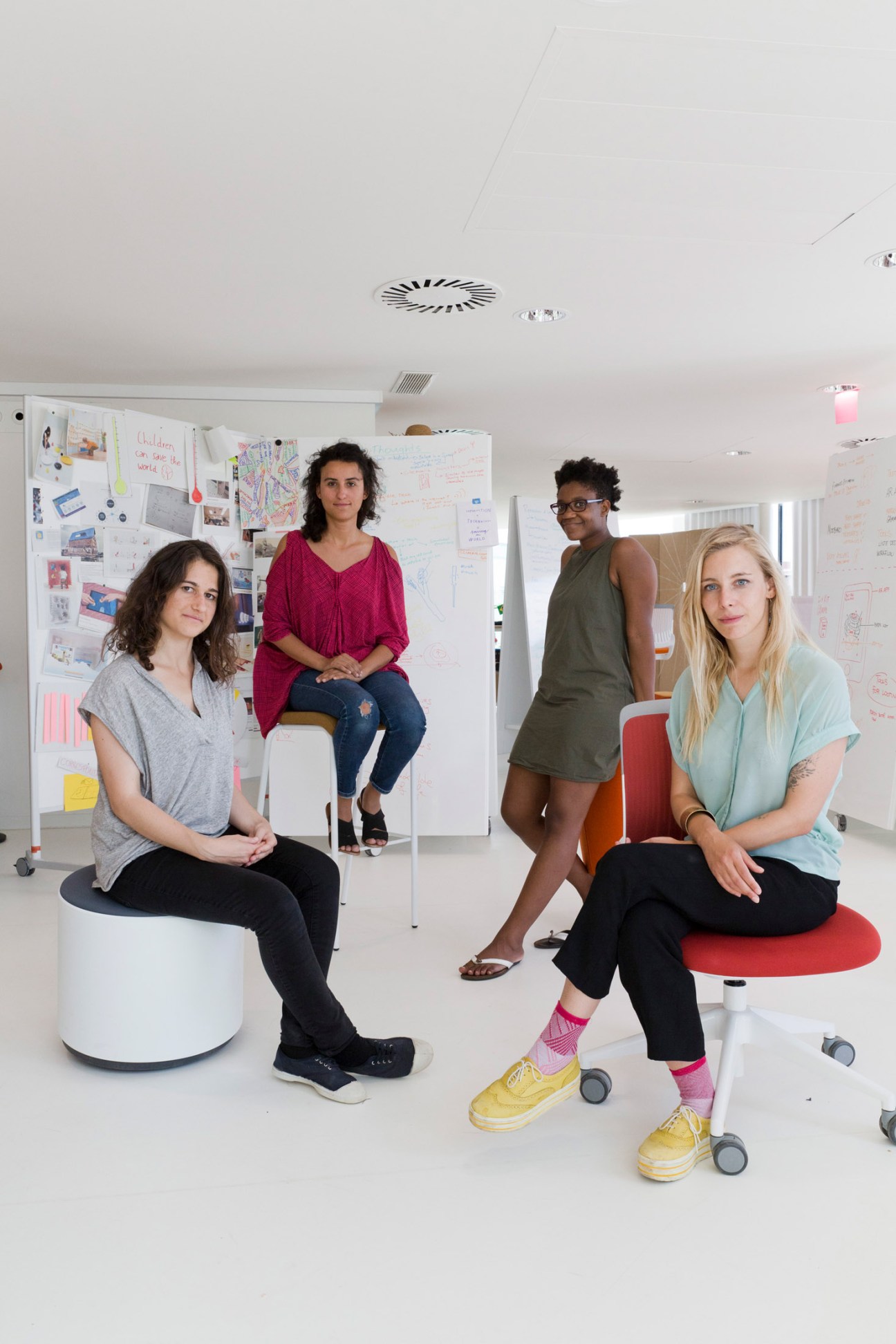 Four young professionals posing in a bright workspace with whiteboards covered in sketches and notes behind them.