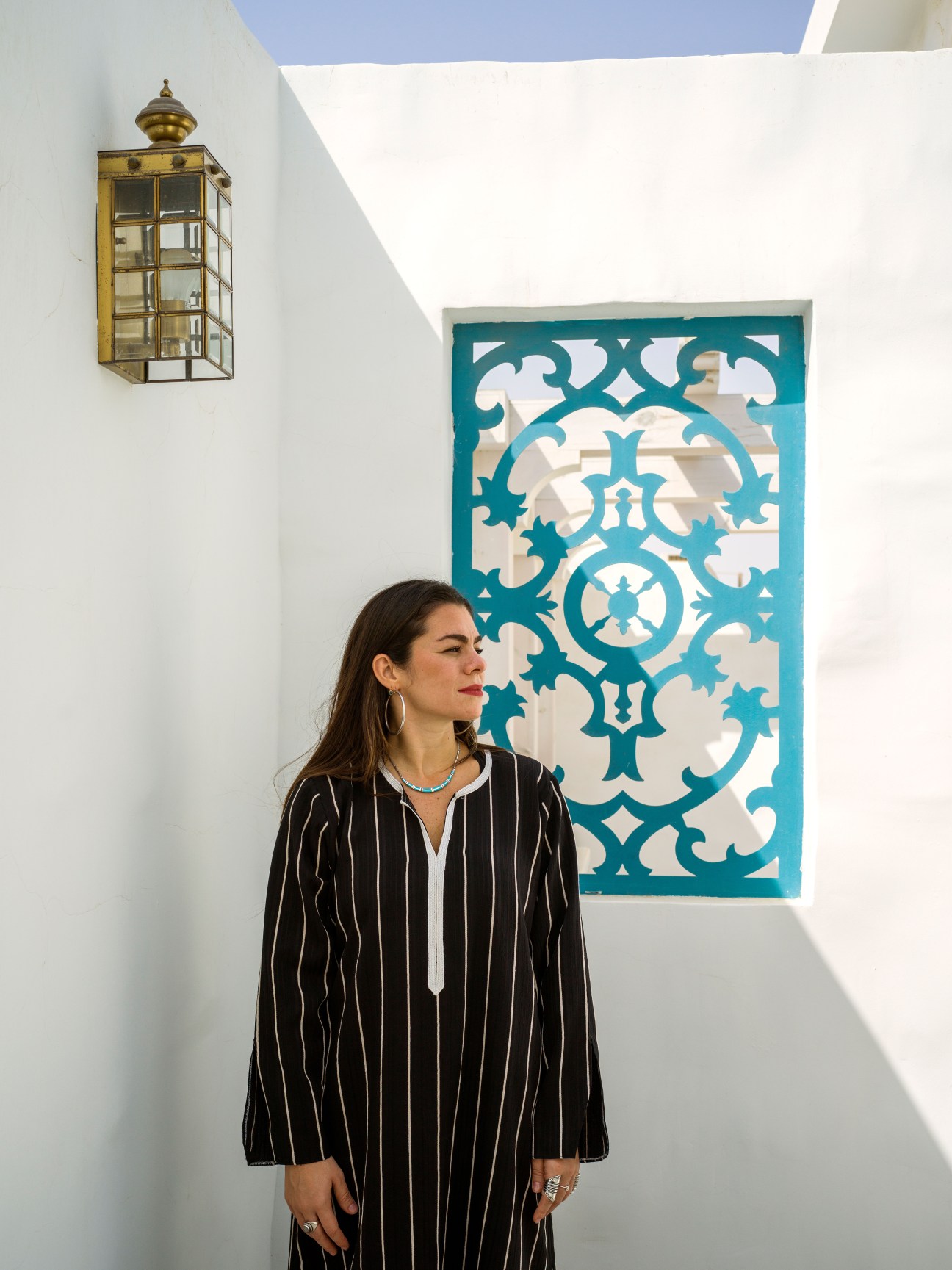 Fashion designer Nasiba Hafiz standing in front of turquoise Islamic geometric artwork in her Jeddah villa.