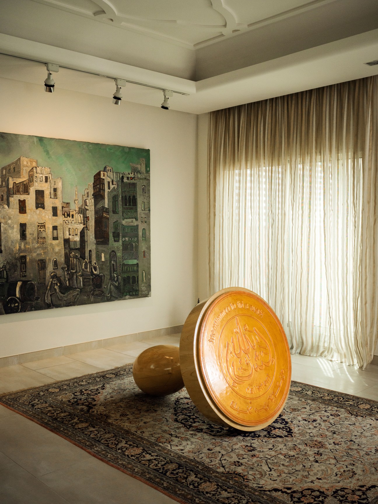 'The Stamp (Amen)' by Abdulnasser Gharem, an illuminated yellow circular sculptural work displayed in a gallery space with traditional artwork on the wall.