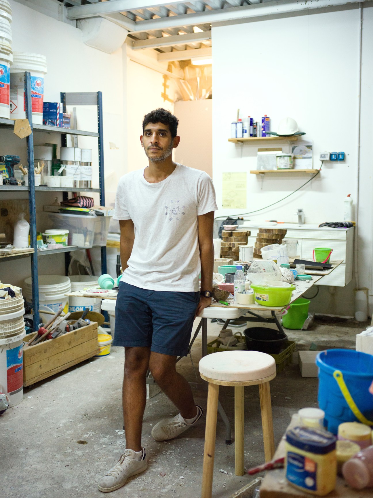 Artist Abdulrahman Gazzaz standing in his studio workspace surrounded by art supplies and materials.