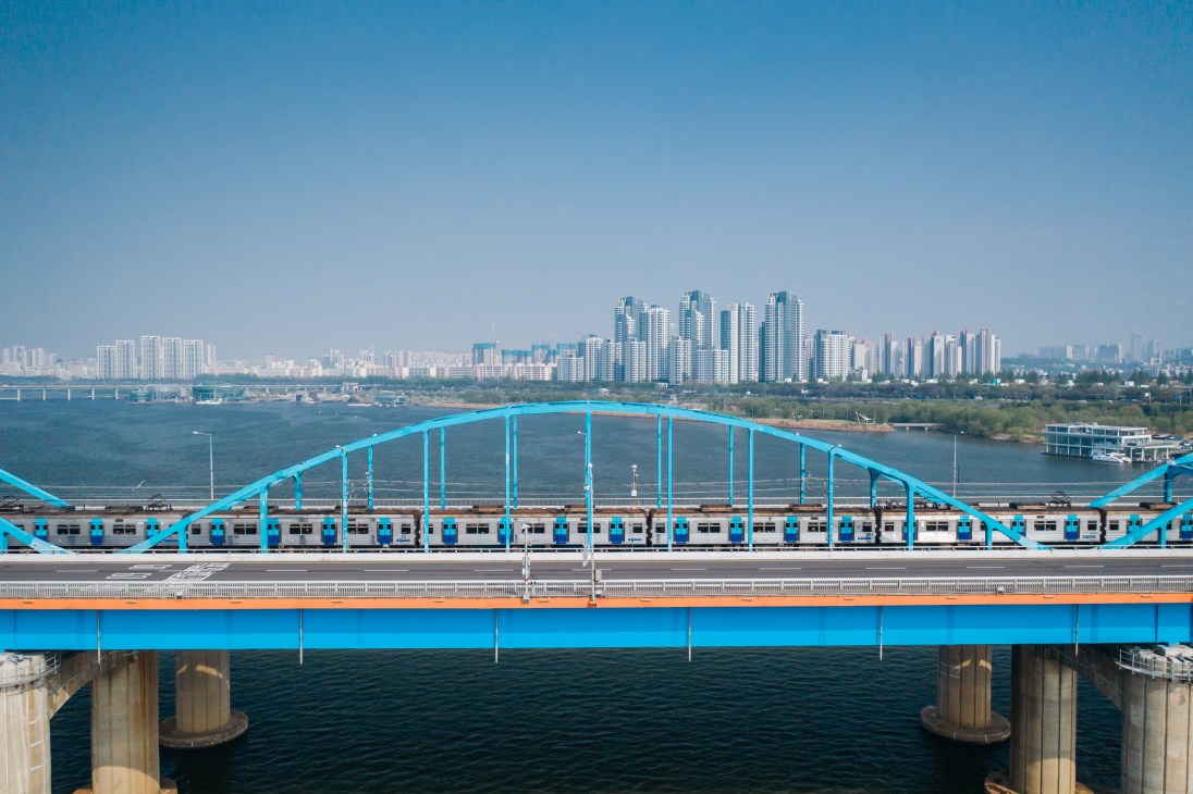 Seoul subway train crossing the bright blue Hannam Bridge over the river with city skyline in background.