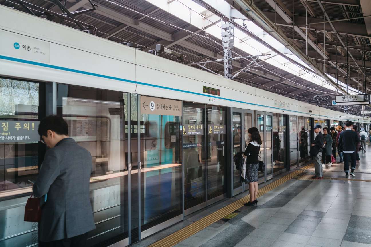 Passengers board and wait at a Seoul Metro subway station platform with modern train doors and signage.