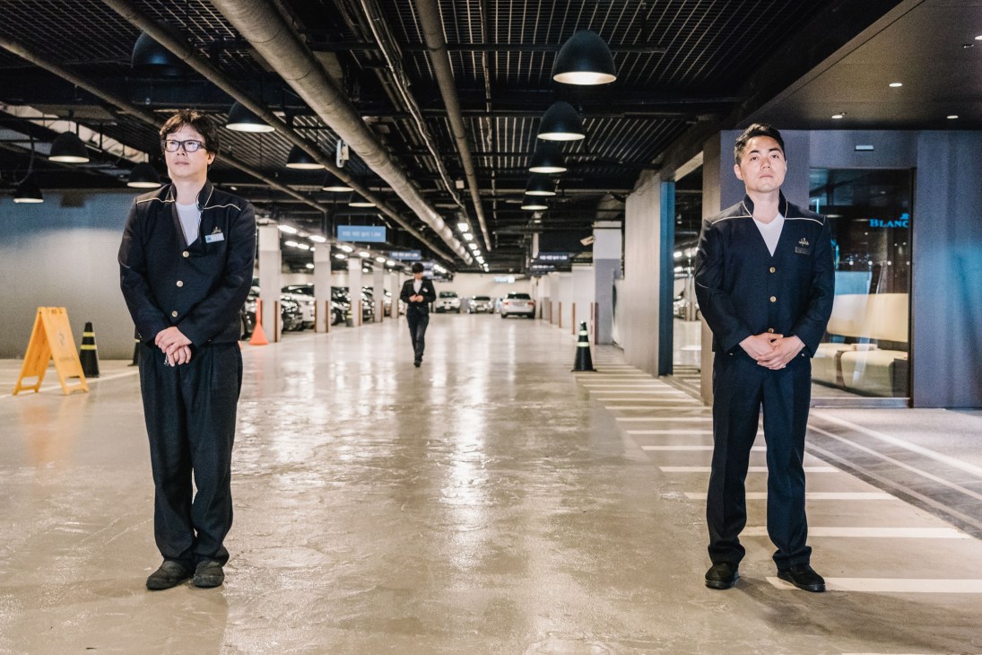 Two valets in dark uniforms stand in an underground parking garage awaiting customers.