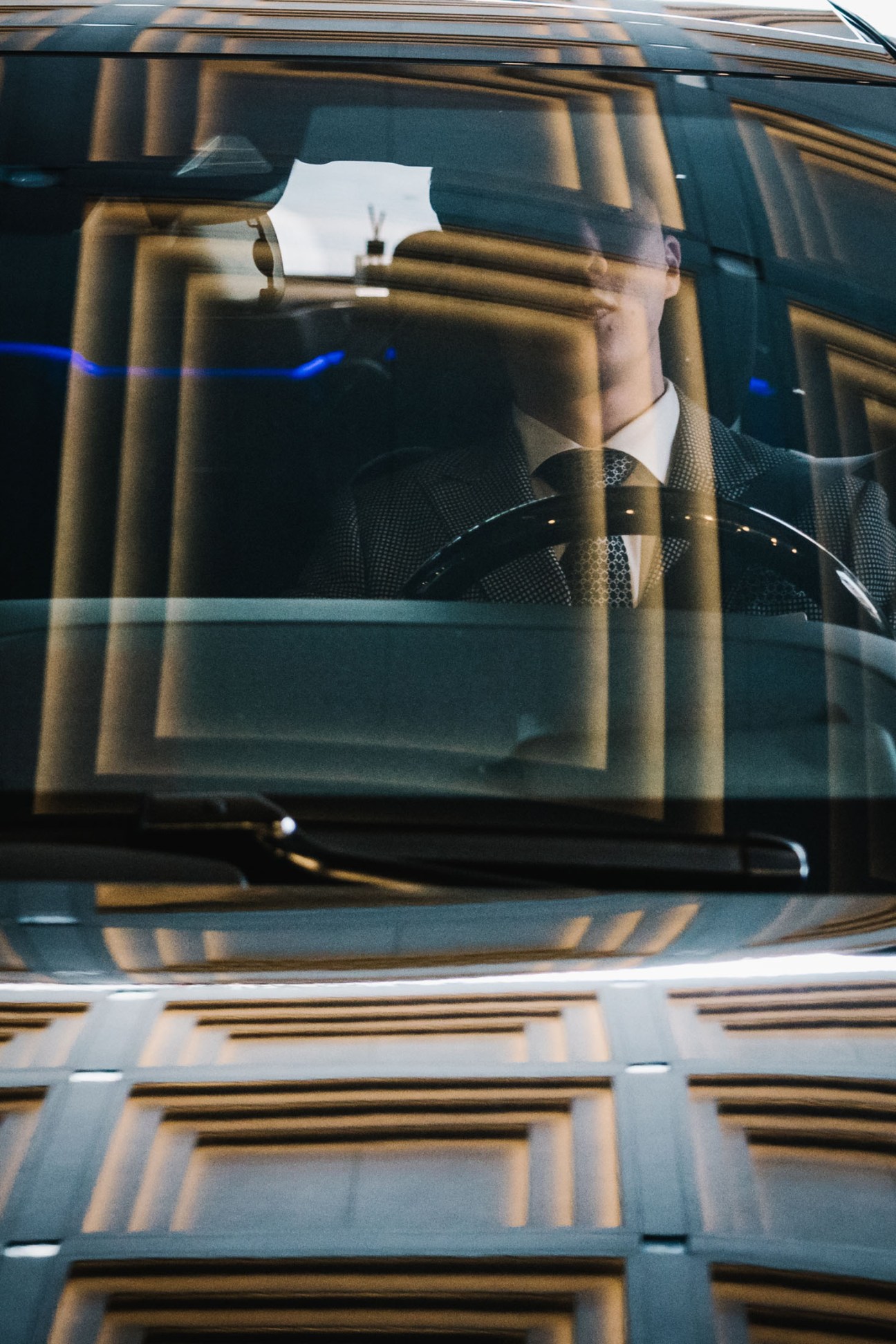 Valet driver in formal suit and tie sits in luxury car with parking ticket on windscreen.