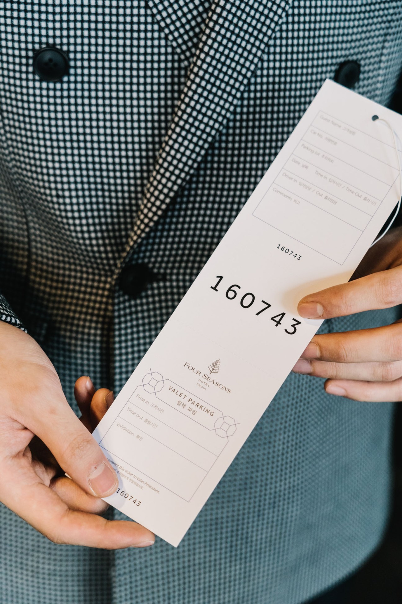 Hands holding a Four Seasons valet parking ticket showing number 160743 against a textured blue fabric background.