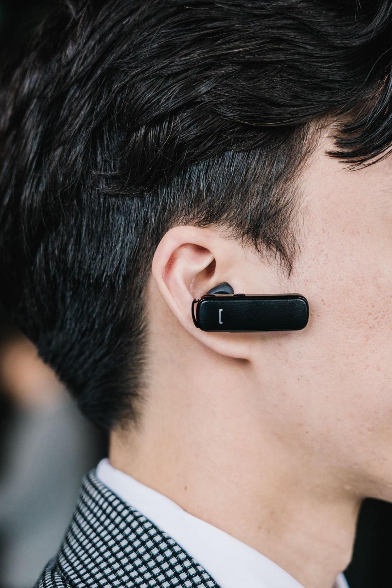 Close-up of a person wearing a black wireless earpiece against their ear.