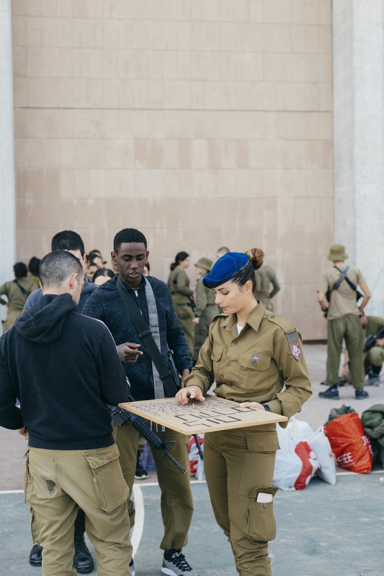IDF soldier in tan uniform with blue beret holding a training diagram while instructing two male trainees.
