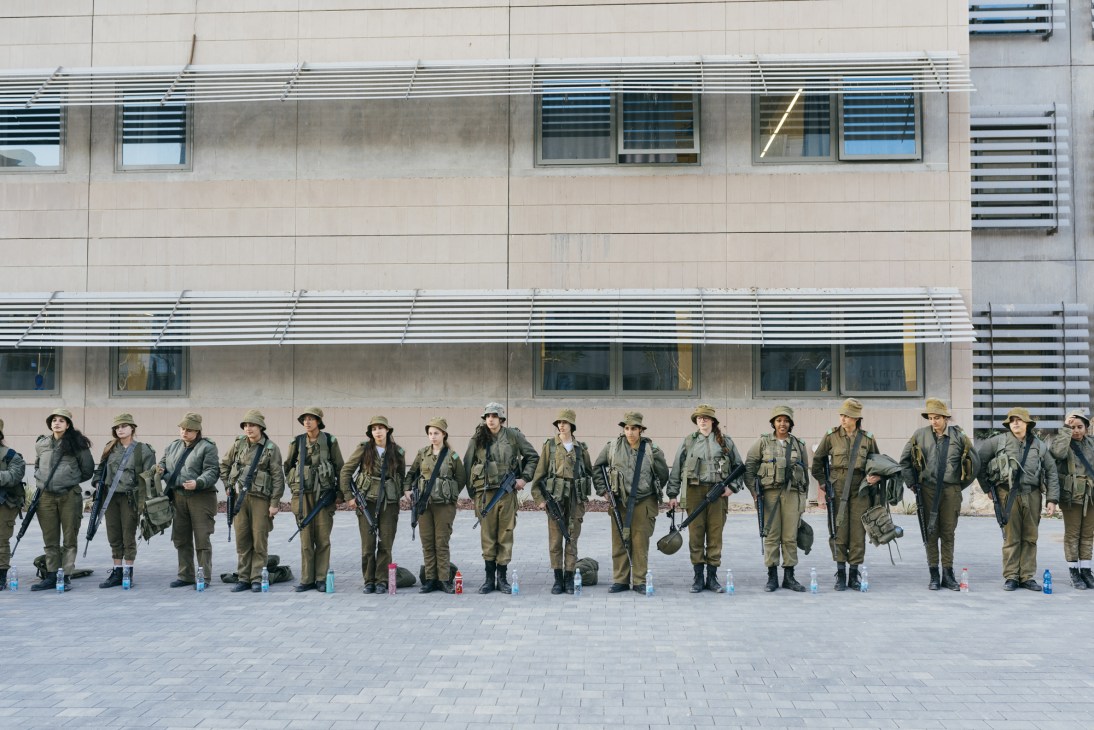 IDF soldiers in uniform standing in a line before a modern military building.