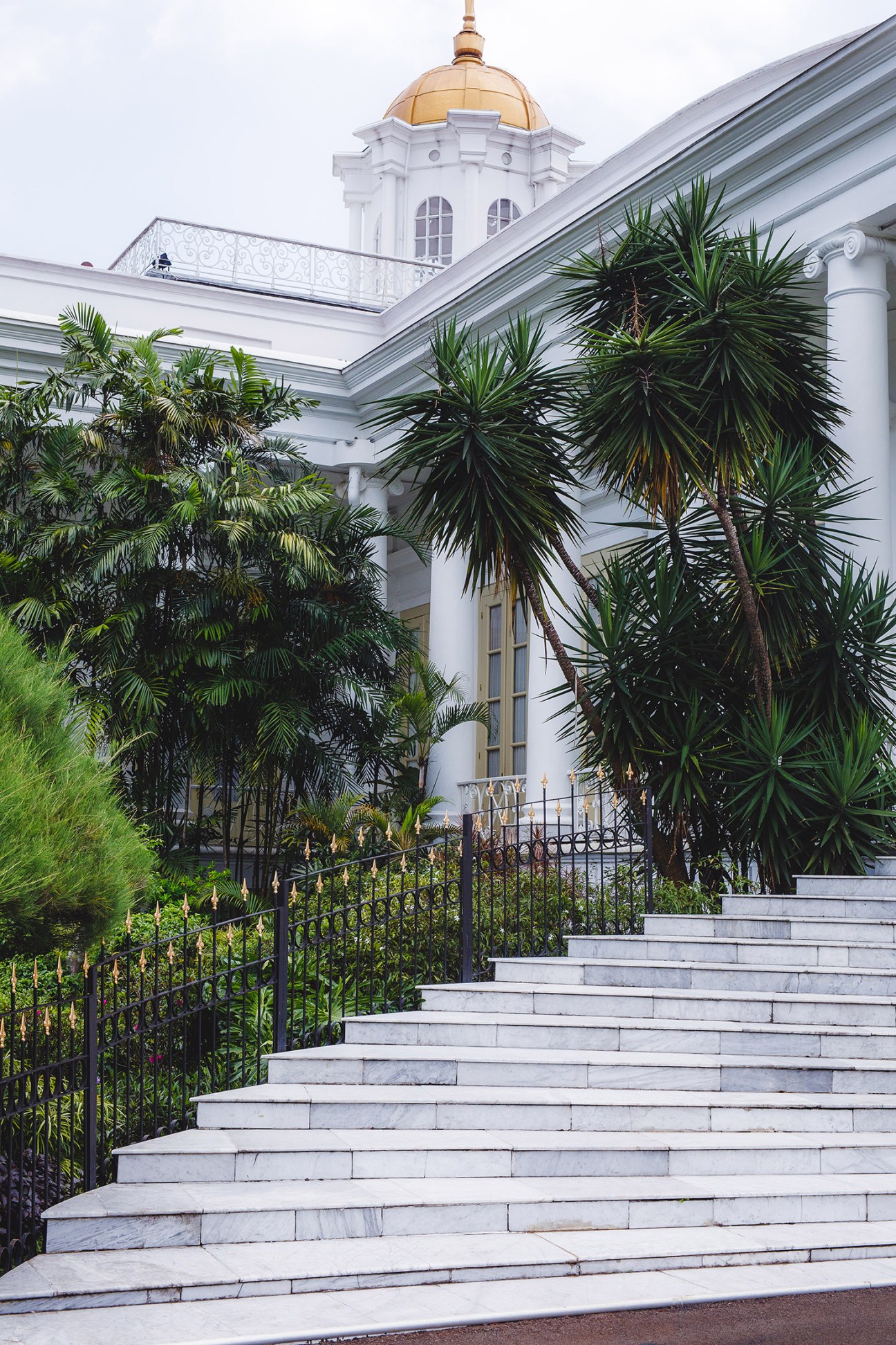 White neoclassical presidential palace building with golden dome, surrounded by tropical palm plants and marble steps.