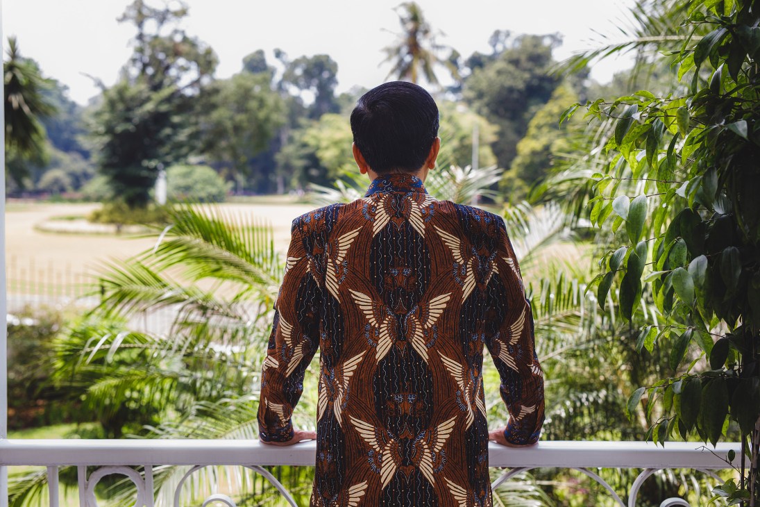 Man in traditional Indonesian batik shirt viewing botanical gardens from palace balcony