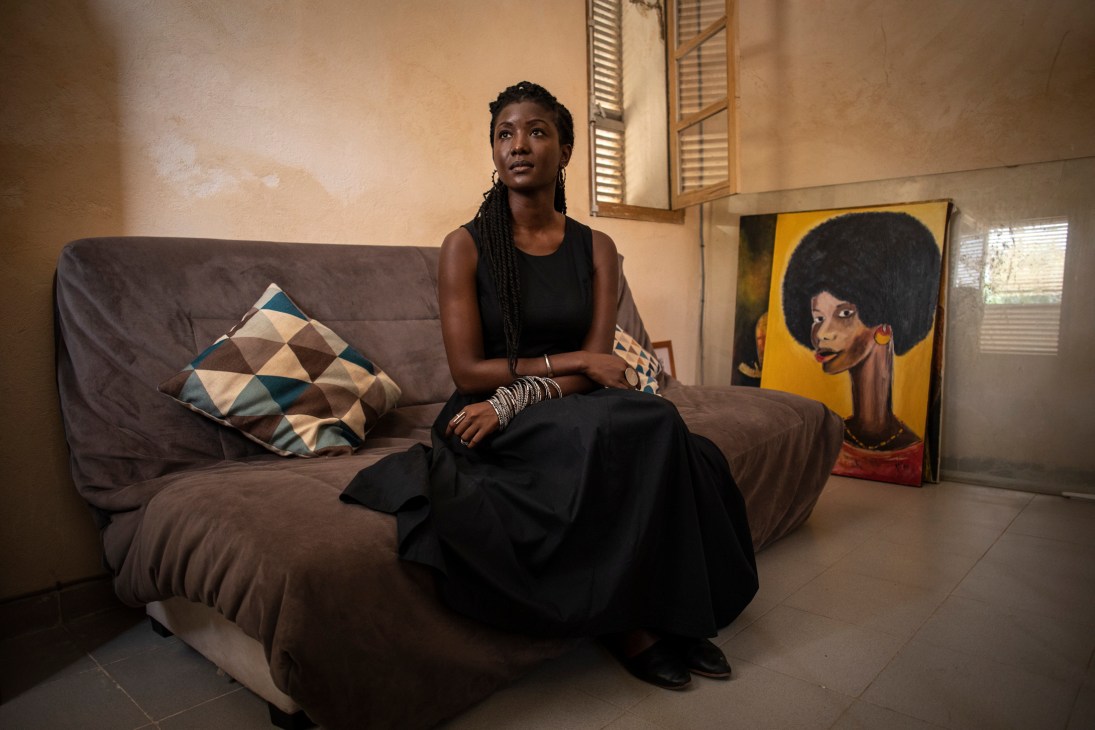 Nzinga Mboup sits on a grey couch in her living room with African artwork on the wall