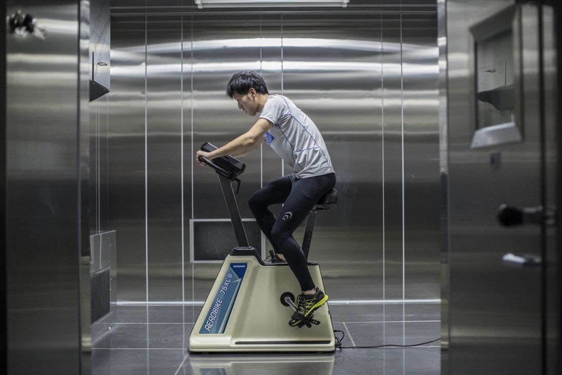 Person exercising on stationary bike equipment in modern laboratory facility with metal panels
