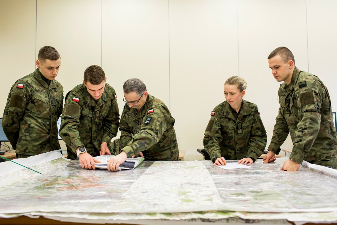Polish military cadets in camouflage uniforms study maps during a training session.