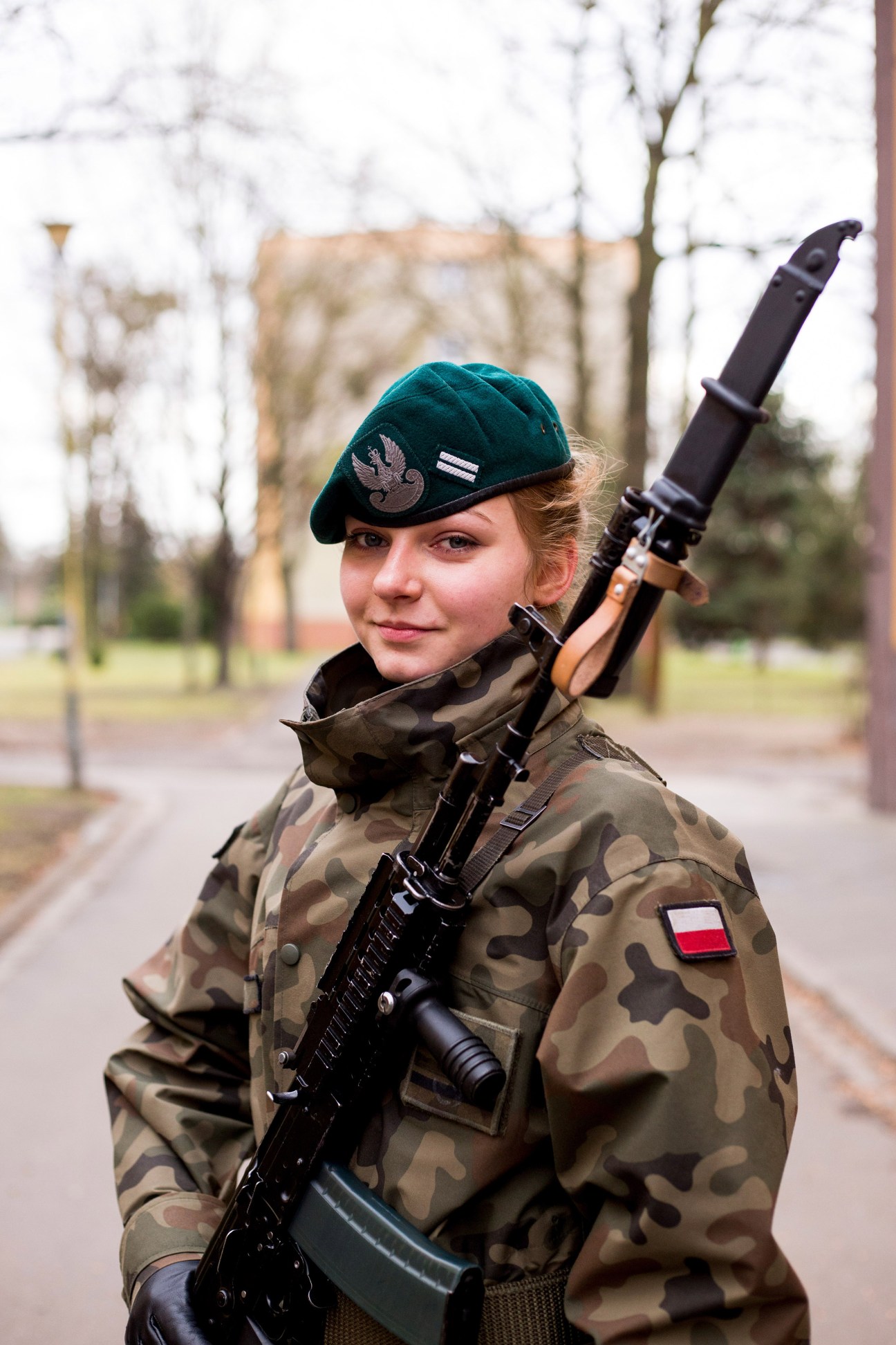 Female cadet in camouflage uniform holding a Polish Beryl assault rifle, wearing a beret with an eagle emblem.