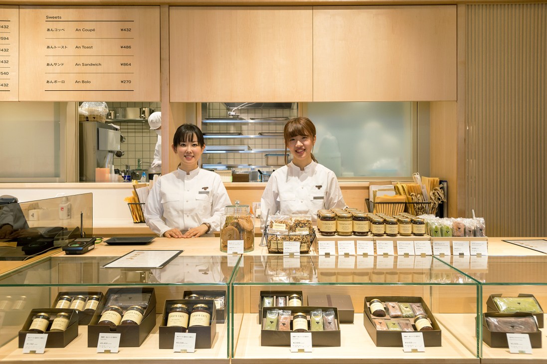 Two staff members in white uniforms stand behind a counter at Toraya Café in Tokyo's Shinjuku area.