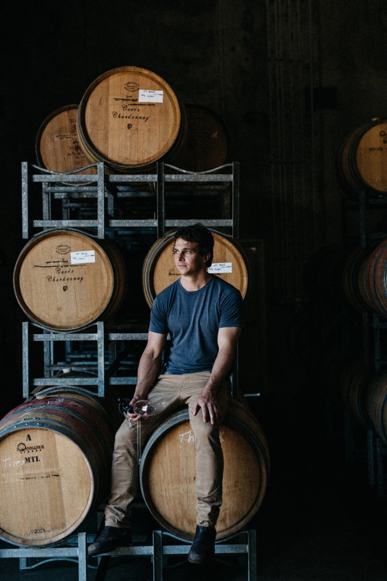 Nic Peterkin sits among stacked wooden wine barrels in his barrel room at Las Vino winery in Margaret River.