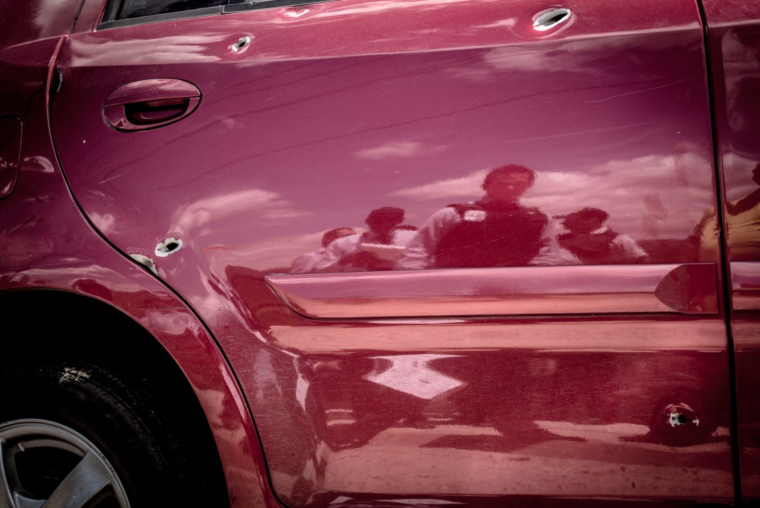 Red car door with damage and scratches reflecting silhouettes of people